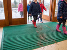 Holly green Frontrunner Entry matting at a primary school entrance with children in wellingtons and mud falling into the open channels