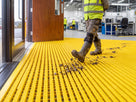 Yellow open-grid entrance matting at a factory personnel door with mud and stones scraped from a work boot into the channels