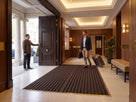 Dark brown open-grid entrance matting in a brass matwell frame at a boutique hotel entrance
