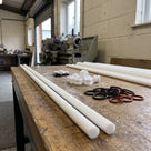 Slim off-white PTFE rods on a timber bench in a seal-making workshop with small turned PTFE bushes and O-rings
