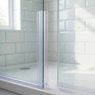 Clear seal gripping the edge of a glass shower panel, concertina web stretching across to the next panel, wet tiles