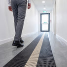 Photoluminescent escape route matting laid down a bright commercial corridor leading to a glazed fire exit door