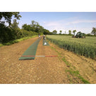 Roll of green grass protection mesh being unrolled along a farm field access track beside a wheat crop