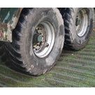 Muddy tractor trailer wheels resting on green grass protection mesh, showing it under heavy farm traffic