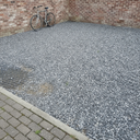 Grey gravel off-road parking area beside a brick garage with the honeycomb grid visible beneath the stone