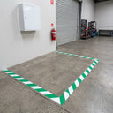 Green and white diagonal striped floor marking tape outlining a keep-clear zone beneath a wall-mounted safety cabinet