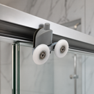 Close-up of a grey plastic twin wheel roller on a glass shower door, both white wheels seated in the rail