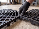 Gloved hand locking two 25mm raised open-grid tiles together by their moulded lock-fit tabs