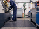 Black open-rib anti-fatigue PVC matting in front of a lathe in a UK machine shop, swarf on the floor