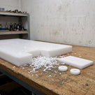 Thick natural white HDPE slab on a workshop bench with a machined wear pad and two spacers cut from it, white swarf around