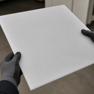 Gloved hands holding a natural white HDPE PE300 sheet in a workshop, square-cut edge visible