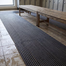 Low angle along the lengthwise ribs of dark grey barefoot matting beside a weathered timber bench, changing room lockers and window behind