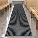 Dark grey Heronrib matting rolled out as a runner down a leisure centre changing room aisle between timber slatted benches and lockers, wet footprints on the tiled floor alongside.