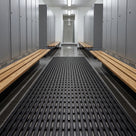 Dark grey Heronrib matting rolled out as a runner down a sports centre changing room aisle between banks of metal lockers and wooden slatted benches.