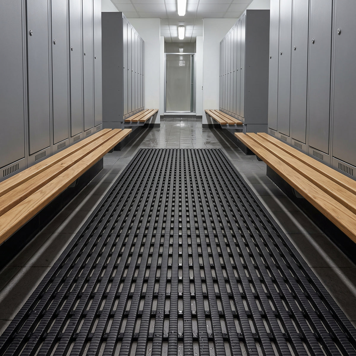 Dark grey matting down a changing room aisle between grey lockers and pale timber benches, glazed door at the end