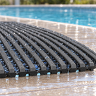 Close detail of dark grey Heronrib matting on a wet poolside, showing the serrated rib crests, the black channelled underbars beneath and the full 10.5mm thickness at the cut edge.