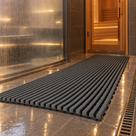 Dark grey Heronrib matting laid as a wet-side walkway across spa flooring between a glass-fronted steam room and a timber sauna door, draining into a floor channel.