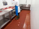 Red grease-resistant open grid matting in a butchery preparation room with offcuts falling through the grid