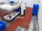 Red open grid matting on the wet floor of a fish processing room, meltwater draining to the floor gully