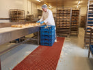 Red open grid anti-fatigue matting along a bakery production and packing line with crumbs falling through