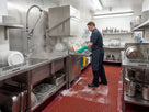 Red open grid matting at a hotel kitchen pot-wash station with soapy water draining through the grid