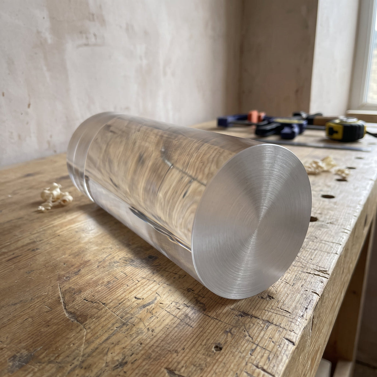 Thick solid clear acrylic rod resting on a rustic timber bench, wood grain showing through the barrel