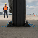 Black rubber aircraft wheel chocks used by ground crew on airport tarmac with rope handles