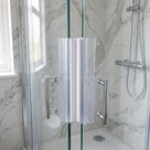 Two clear seals meeting down the edge of wet glass shower doors, white housing strip visible, marble tiles behind