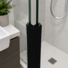 Black magnetic seals closing a glass shower door edge at 135 degrees, basin unit to the left, tiled tray and drain behind
