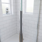 Bright chrome seal running full height where shower glass meets, white metro tiles and chrome valve behind