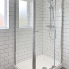 Chrome-framed corner shower enclosure closed, white metro tiles, chrome riser rail and a white tray