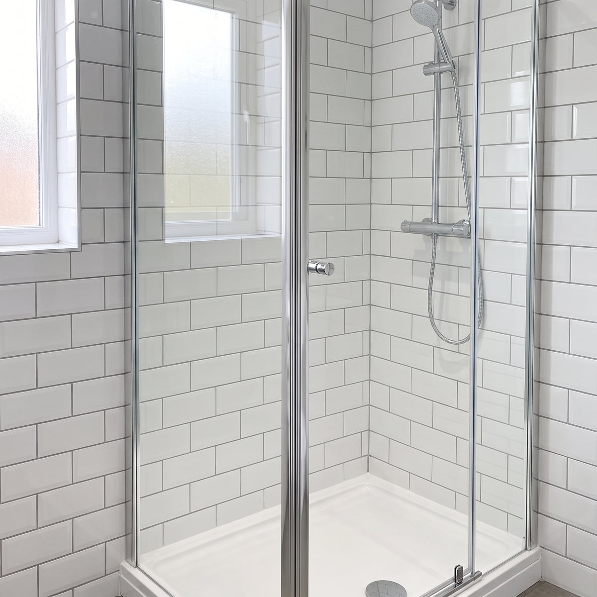 Chrome-framed corner shower enclosure closed, white metro tiles, chrome riser rail and a white tray