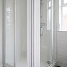 White-framed quadrant enclosure with curved sliding doors closed, white metro tiles and a window right