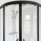 Closed black-framed quadrant shower enclosure with curved head rail, chrome riser rail and window behind
