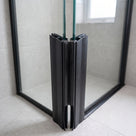 Black seals meeting at the 90 degree corner of a black-framed glass enclosure, grey tiles behind
