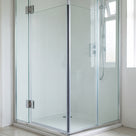 Frameless glass shower enclosure with chrome hinges in a white bathroom, seal not visible at this distance