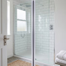 Glass shower door closed against a chrome post in a metro-tiled bathroom, seal line down the join