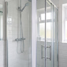 Bifold glass shower door closed in a white metro-tiled bathroom, a pale seal line down the join