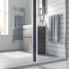 Black seal down the closing edge of a glass shower door, white-tiled bathroom and towel rail behind