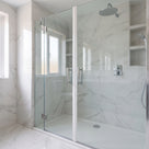 Marble-tiled shower with twin glass doors closed, a white seal line down the centre join, chrome handles