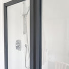Dark-framed shower door closed against a fixed panel, chrome mixer and riser rail behind, white tiled walls