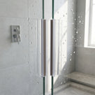 Two clear seals with brown-grey magnet strips meeting on wet glass shower door edges, grey tiles behind