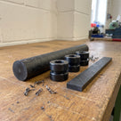Black-grey MoS2 filled nylon rod on an oak bench with stacked turned bushes, a flat wear strip and curled swarf