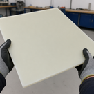 Grey knit gloves lifting a large cream nylon 6.6 panel in a workshop with blue benches behind