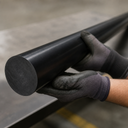Black nylon rod held by gloved hands on a steel bench in a workshop