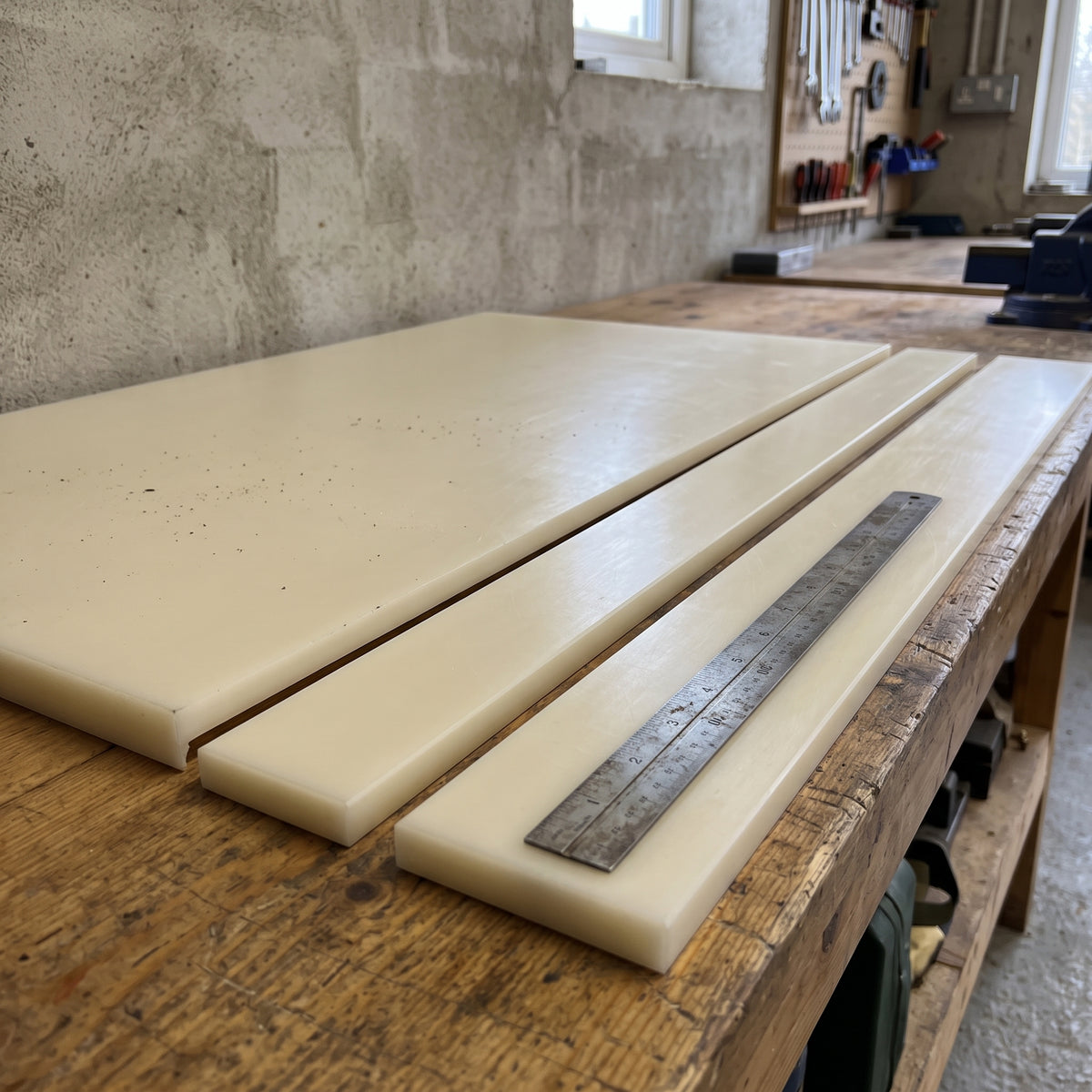 Cream nylon 6.6 sheet on a workbench with two flat wear strips cut from it and a steel rule, tool board behind