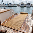 Beige open-grid matting part-unrolled across the timber aft deck of a boat moored at a marina