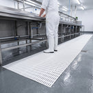 White open-grid matting on the wet floor of a food preparation area in front of stainless steel wash benches