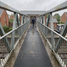 Black fine-ribbed open-grid matting laid along a galvanised steel footbridge to a railway station on a wet day