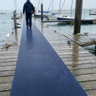 Oxford blue fine-ribbed open-grid matting laid as a walkway strip along a wet timber jetty at a sailing club